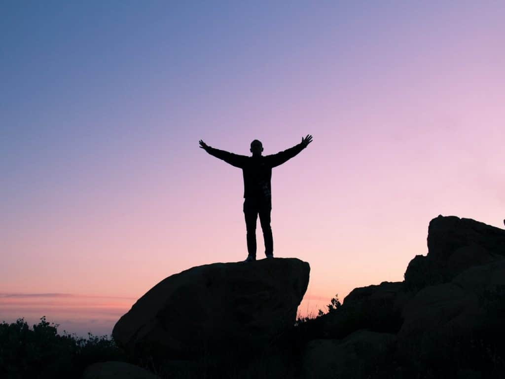 silhouette of person standing on rock with their arms out